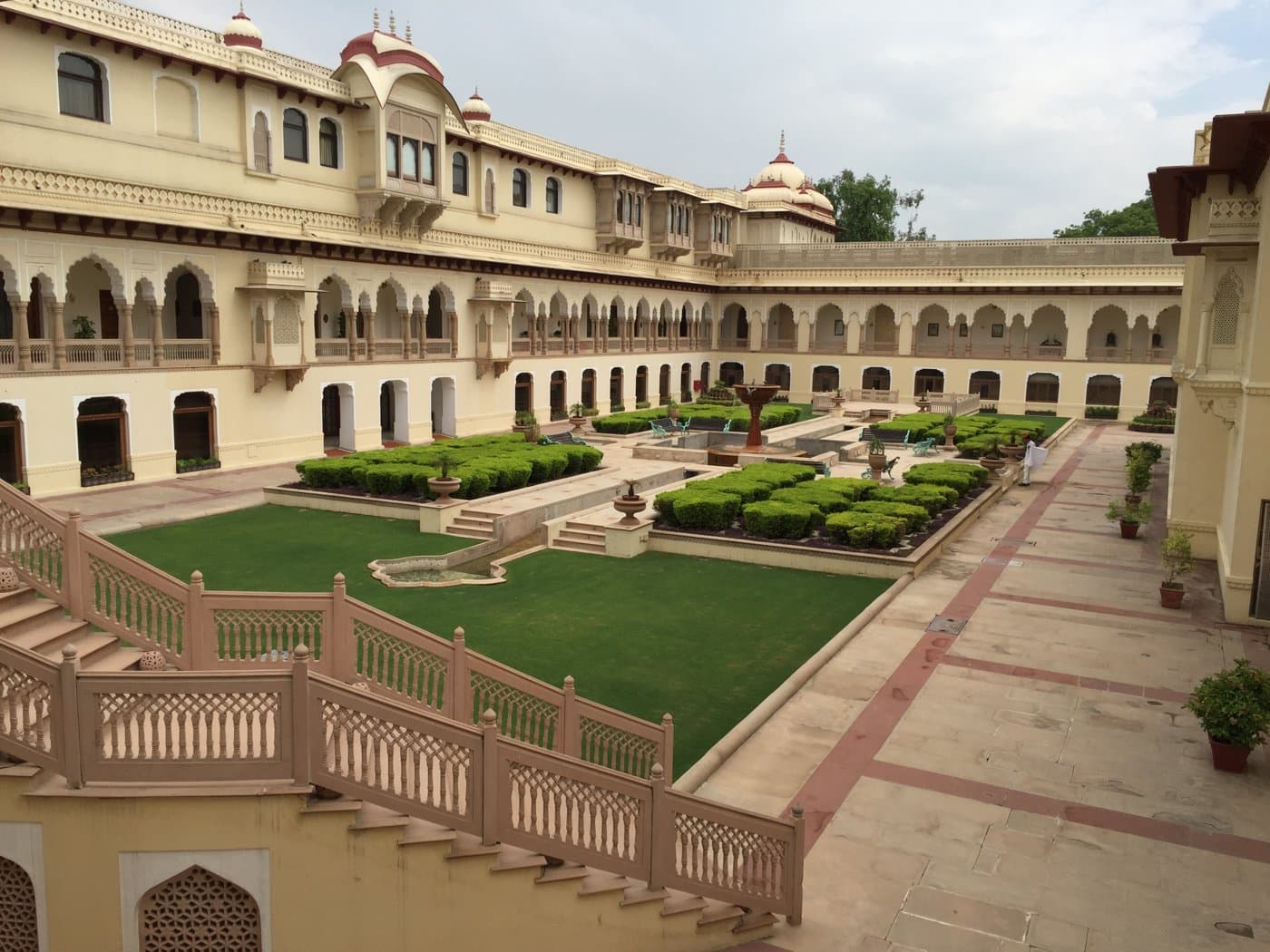 Sunlit Jaipur palace courtyard with green lawns and traditional arches; illustrative photograph